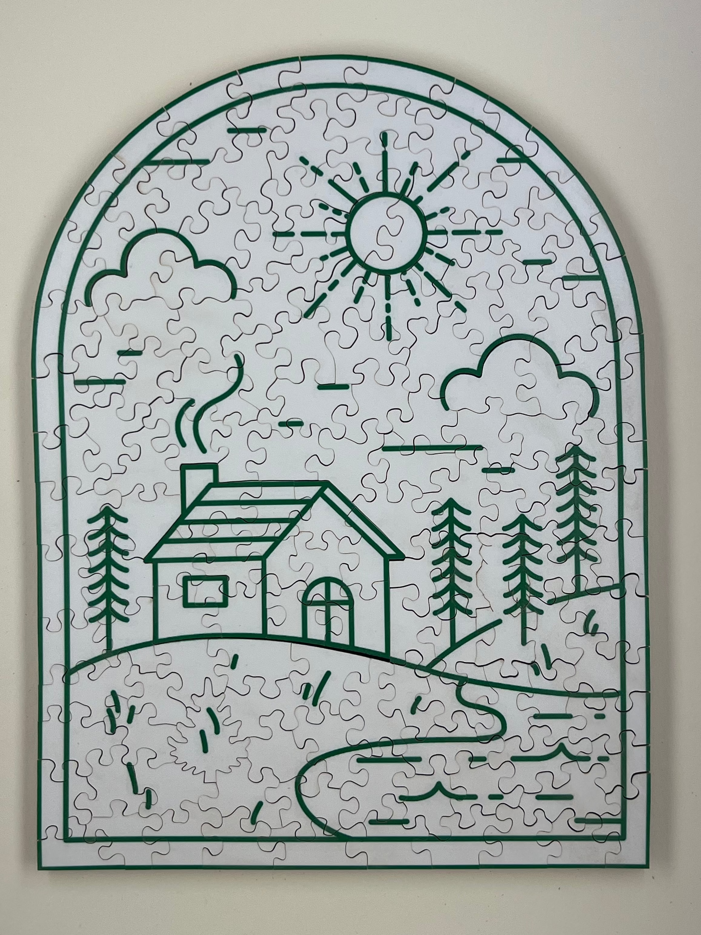 A completed wooden jigsaw puzzle depicting a cabin with surrounding nature, such as trees and a sun illustration, in a curved shape.