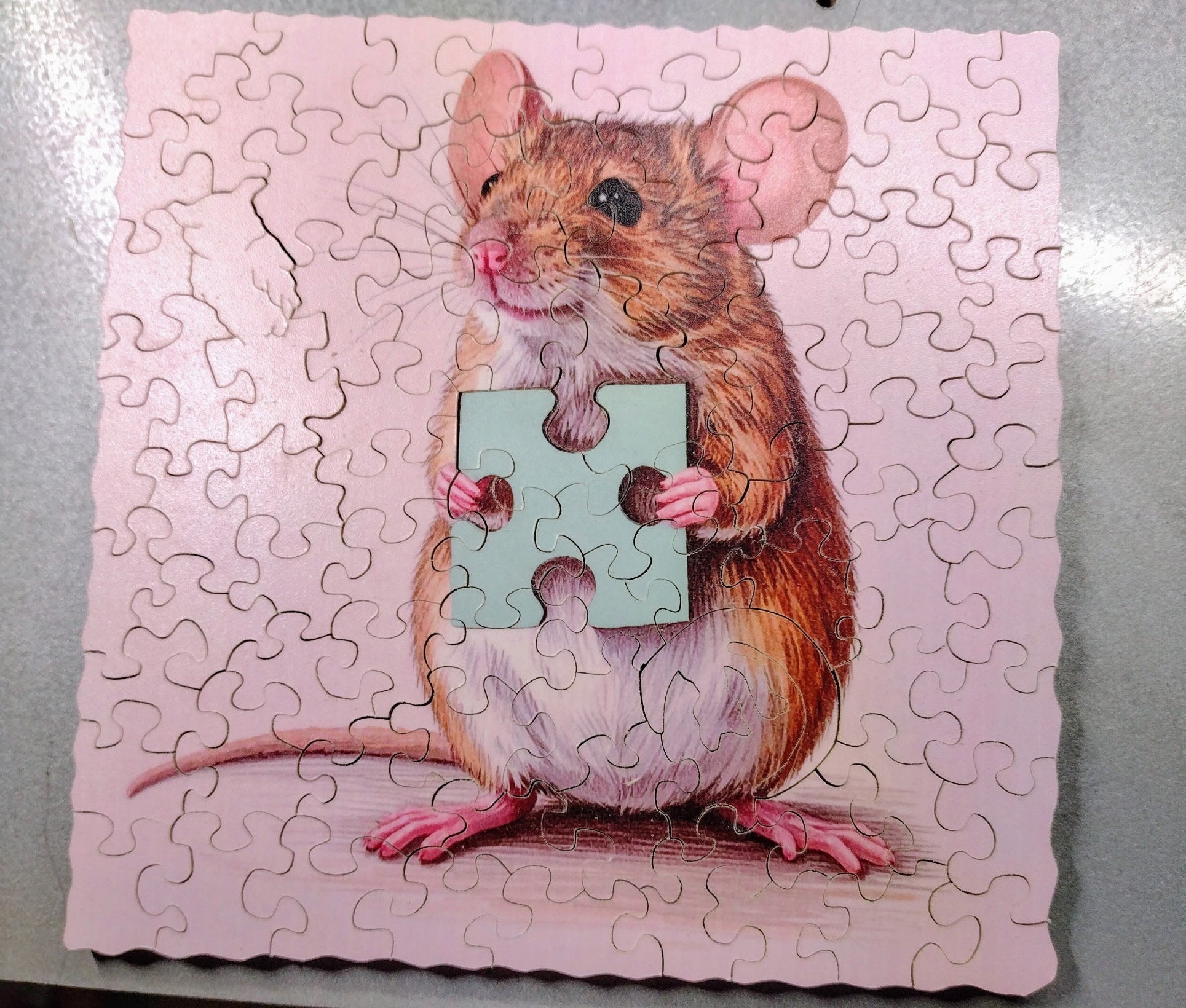 Jigsaw puzzle of a mouse holding a puzzle piece on a pink background
